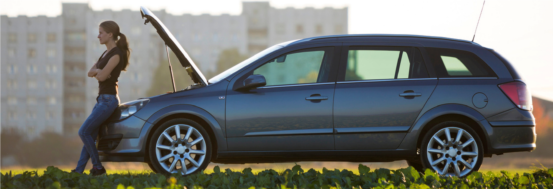 A silver car with its hood open, parked by the roadside beside a person standing near the front.