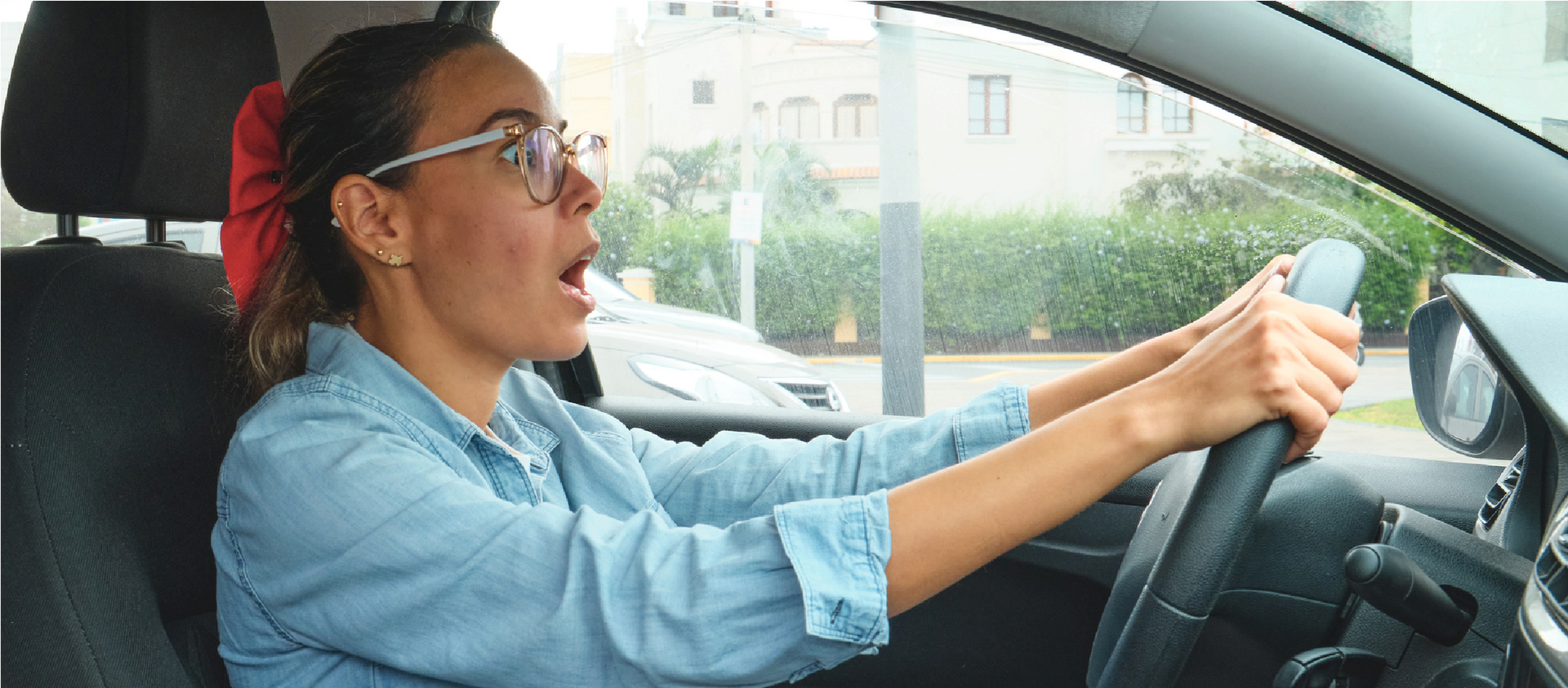 Woman driving a car with her hands on the wheel, looking ahead and speaking indoors in daylight