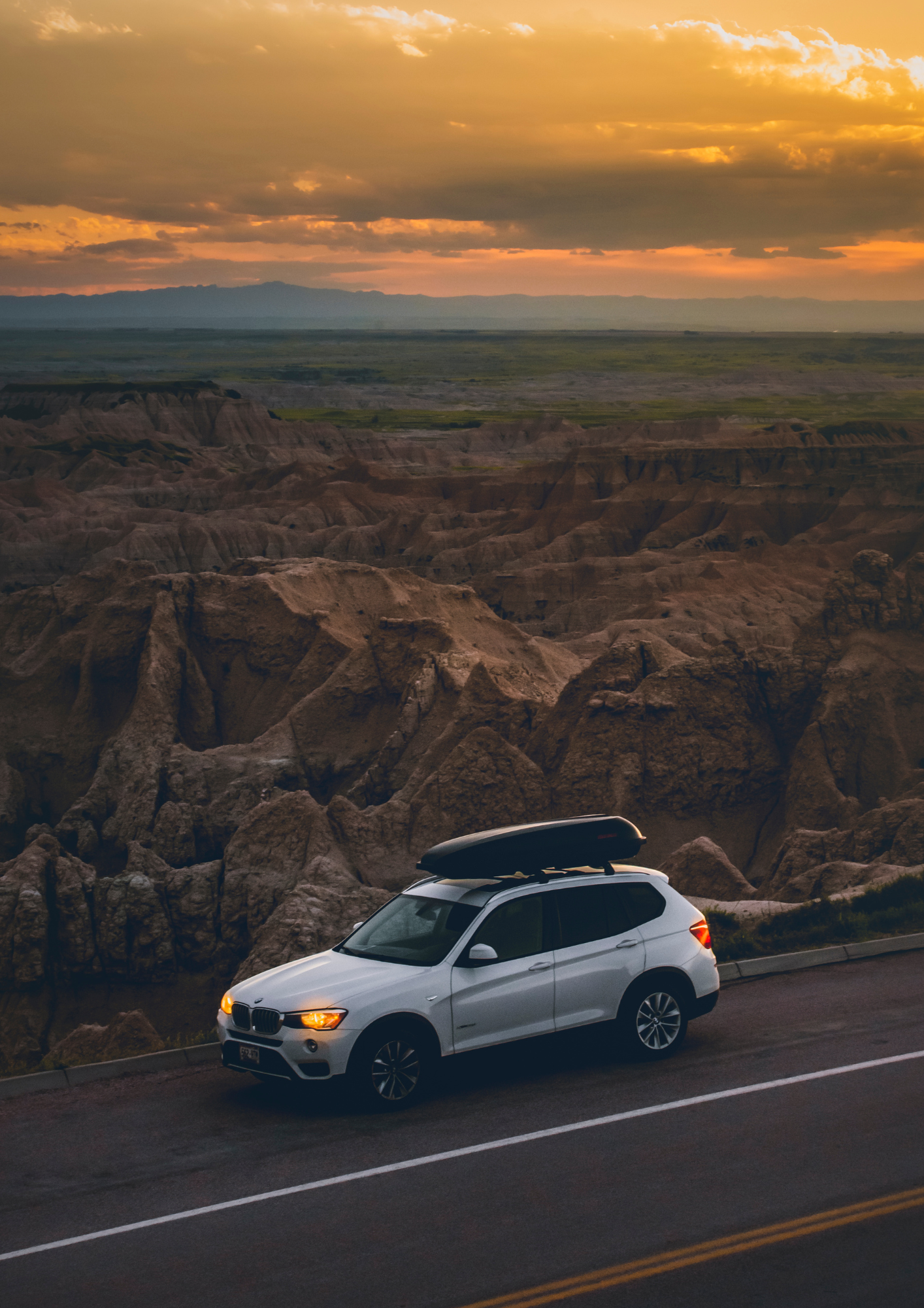 White SUV with roof cargo on a roadside overlooking a canyon at sunset