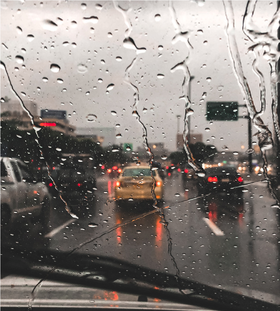 Rainy highway traffic seen through a windshield with raindrops, cars ahead, and wet road reflections.