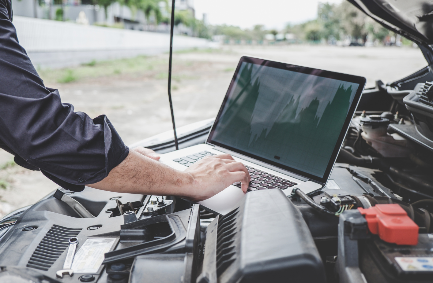 Person working on a laptop in an open car engine bay outdoors