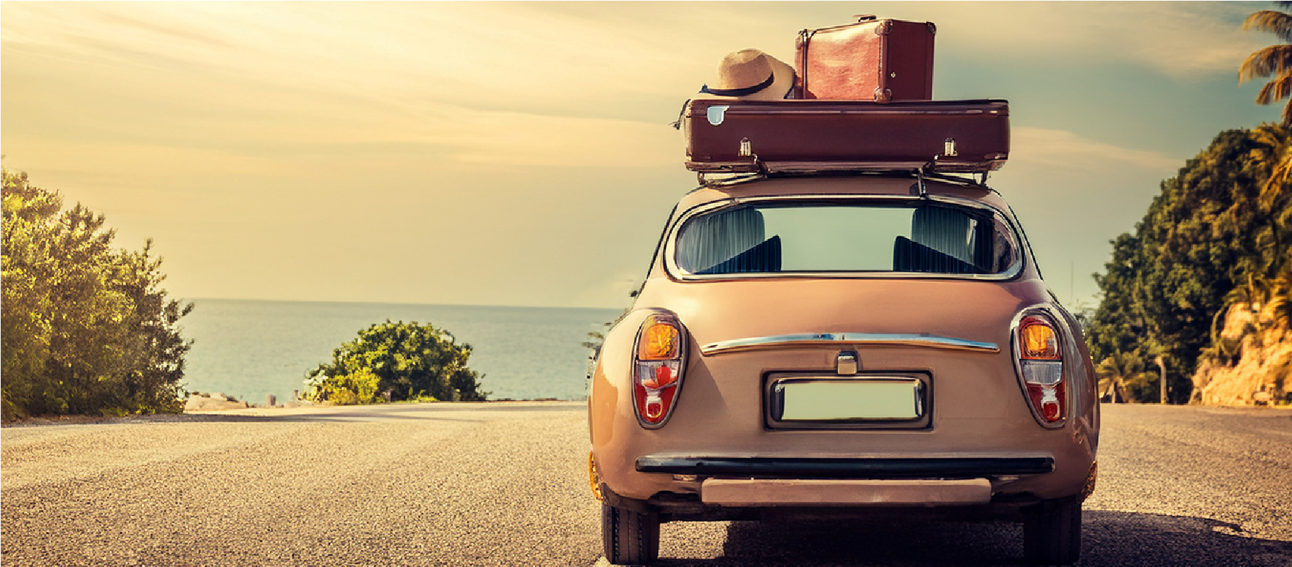 Small car with luggage on the roof parked on a coastal road at sunset