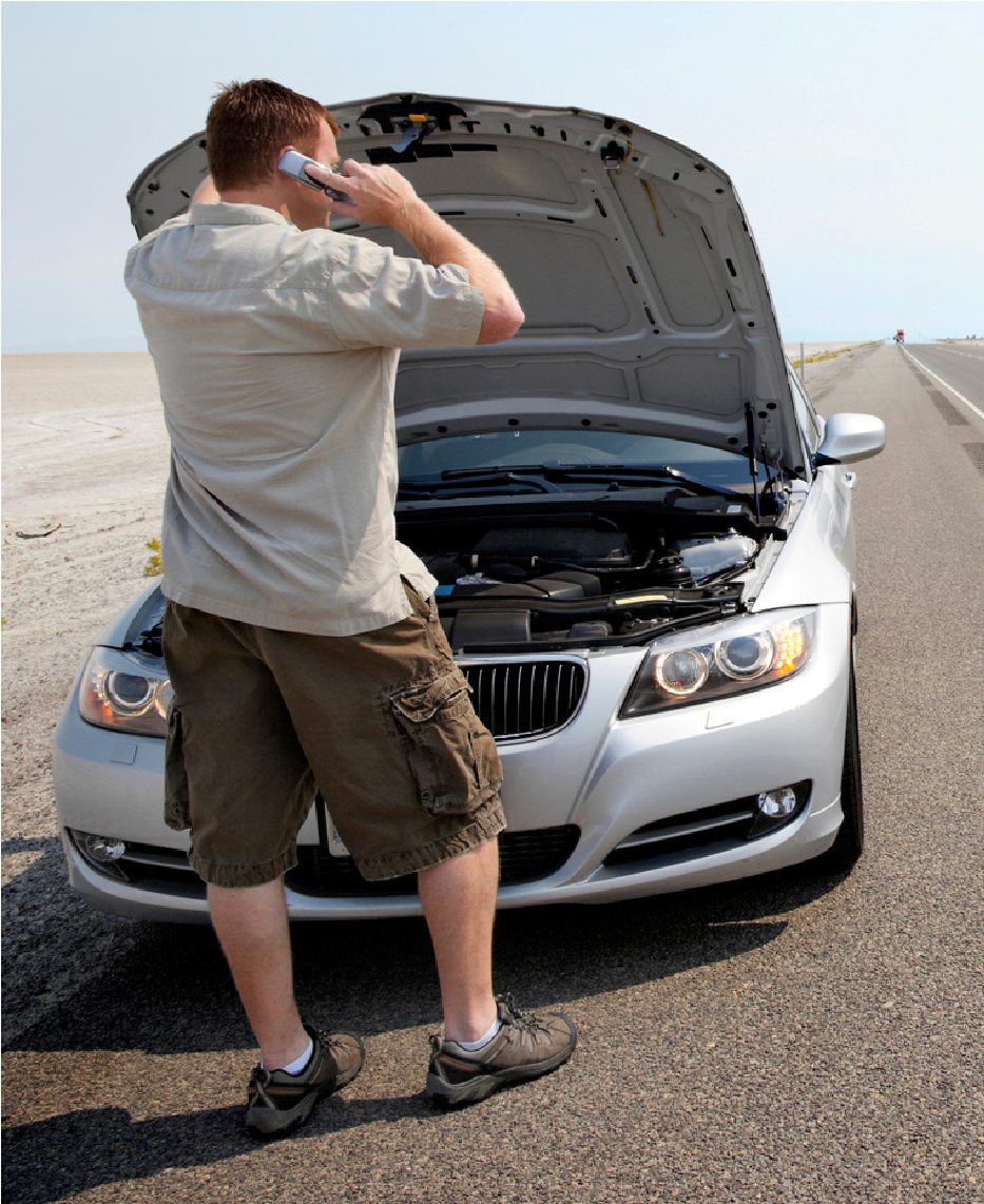 Man standing by a silver car with hood open on a roadside, looking into the engine compartment.