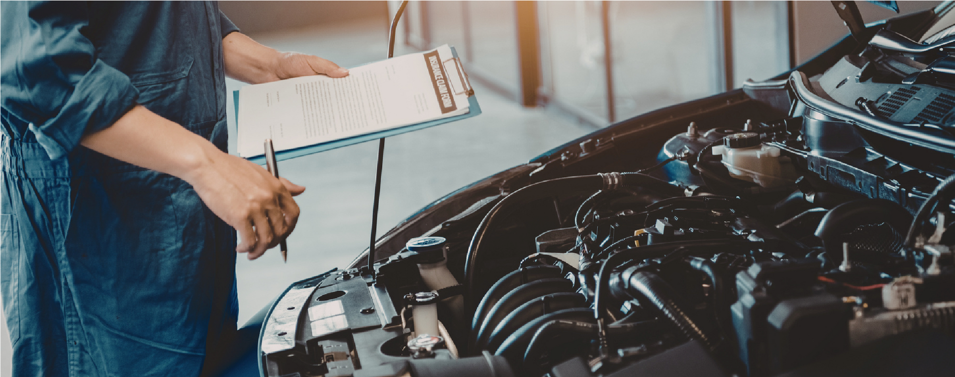 Mechanic in blue overalls inspecting a car engine with a clipboard in a garage
