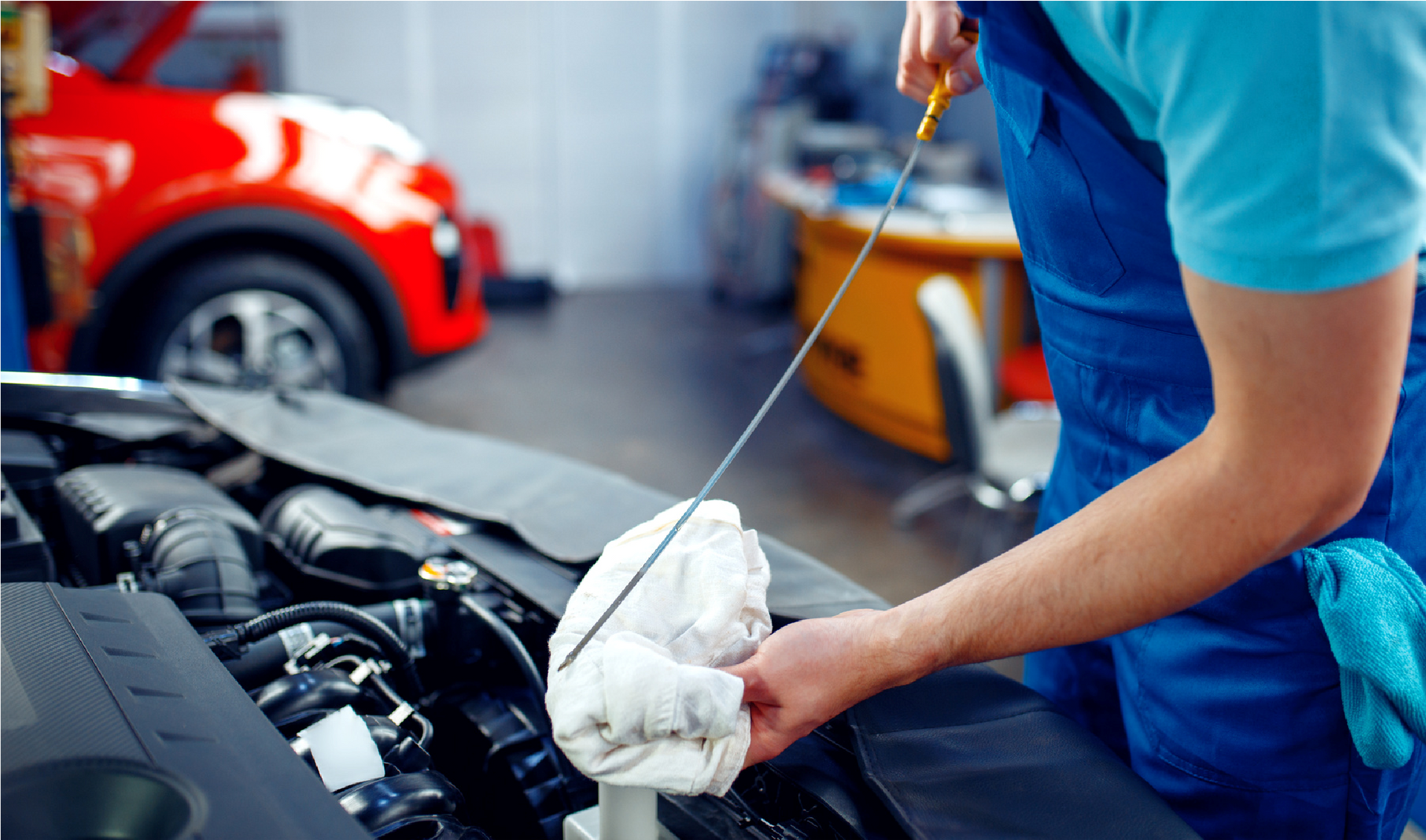 Mechanic checking engine oil with a dipstick in a garage, wearing blue shirt and gloves