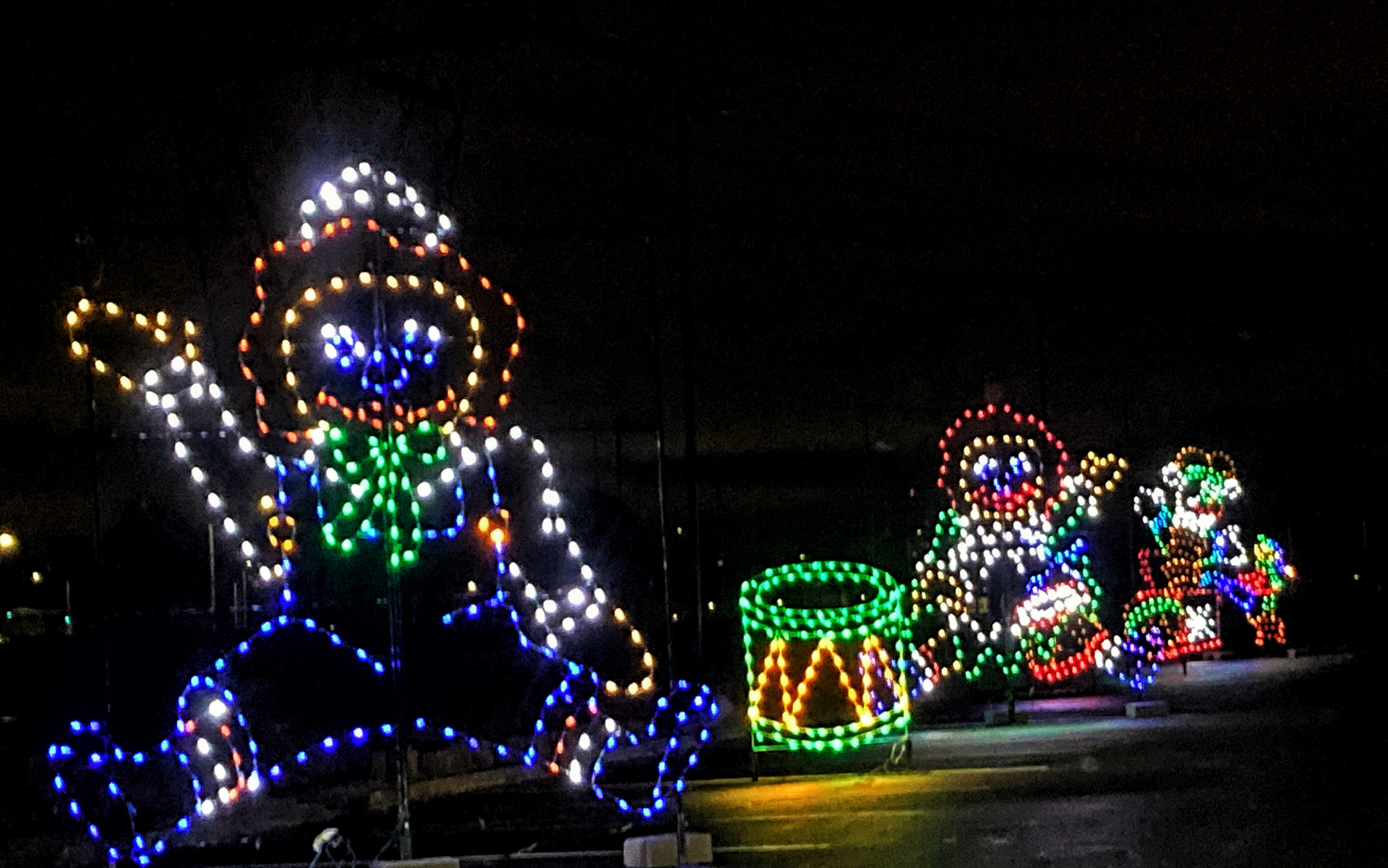 Colorful holiday light display of cartoon musicians, including a drumming figure and glowing instruments at night