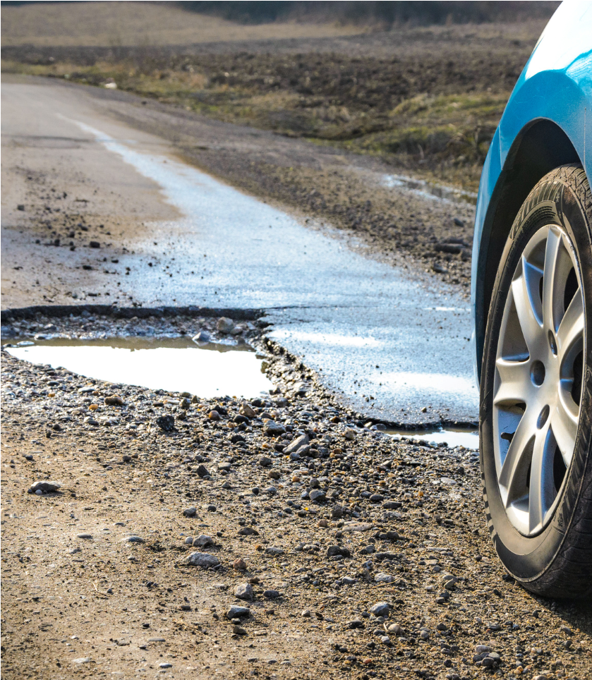 Car tire beside a muddy roadside puddle on a wet rural road