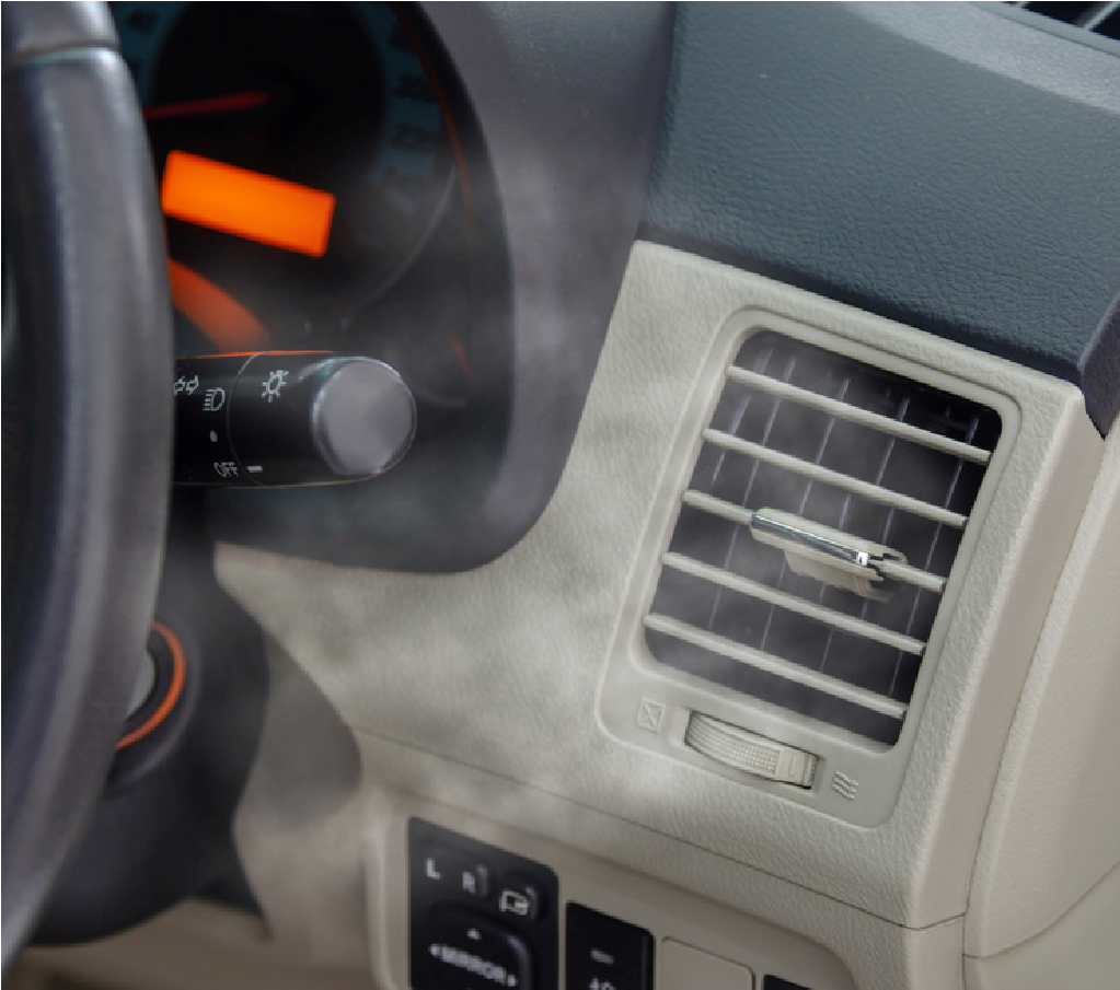 Car dashboard with steering wheel, air vent, and control knobs, with steam or fog drifting across the panel
