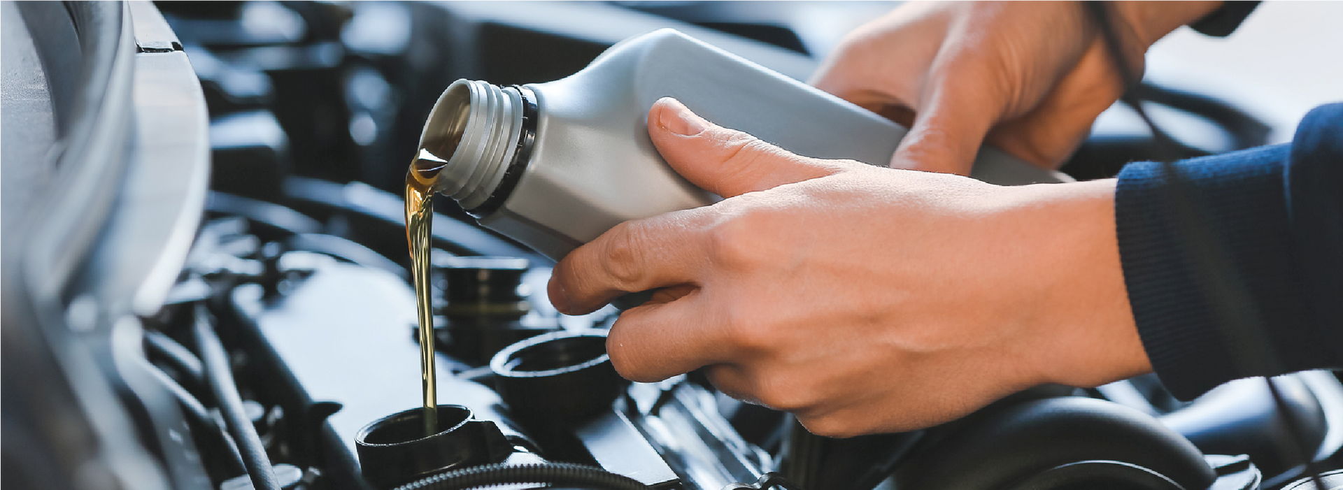 Hands pouring fluid from a bottle into a car engine compartment during maintenance