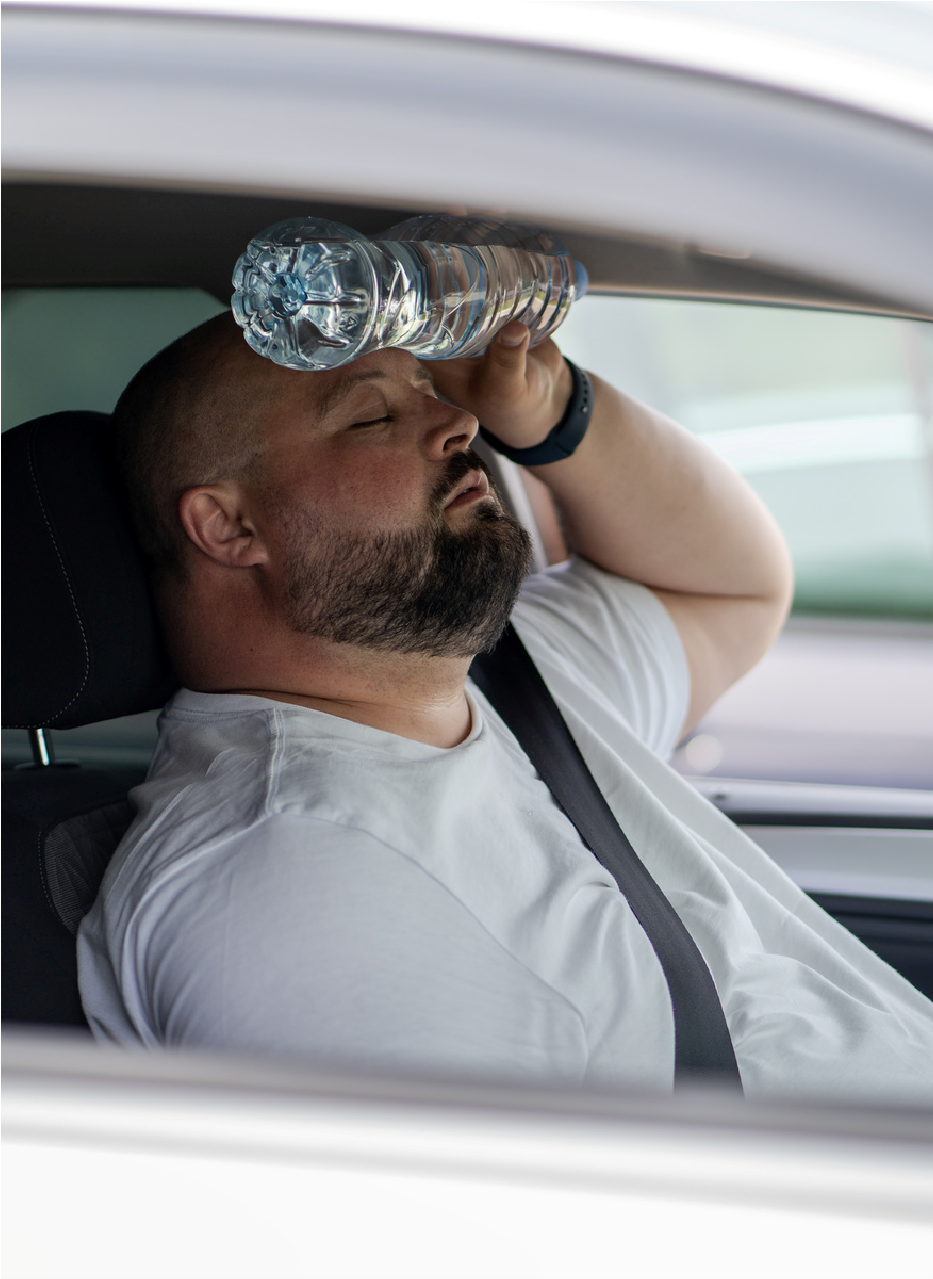Driver in a car drinking from a water bottle while resting his head on his arm