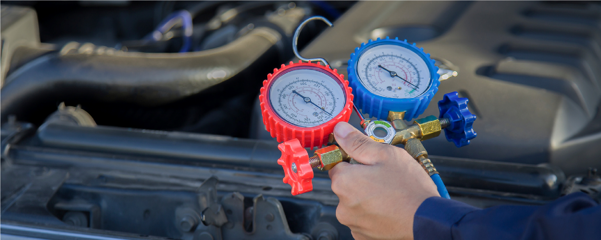 A person holding red and blue manifold gauges over an open car engine bay