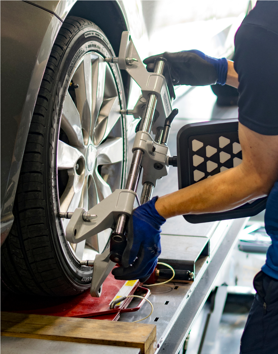 Technician adjusting wheel alignment on a silver car in a garage, using a mounted alignment machine