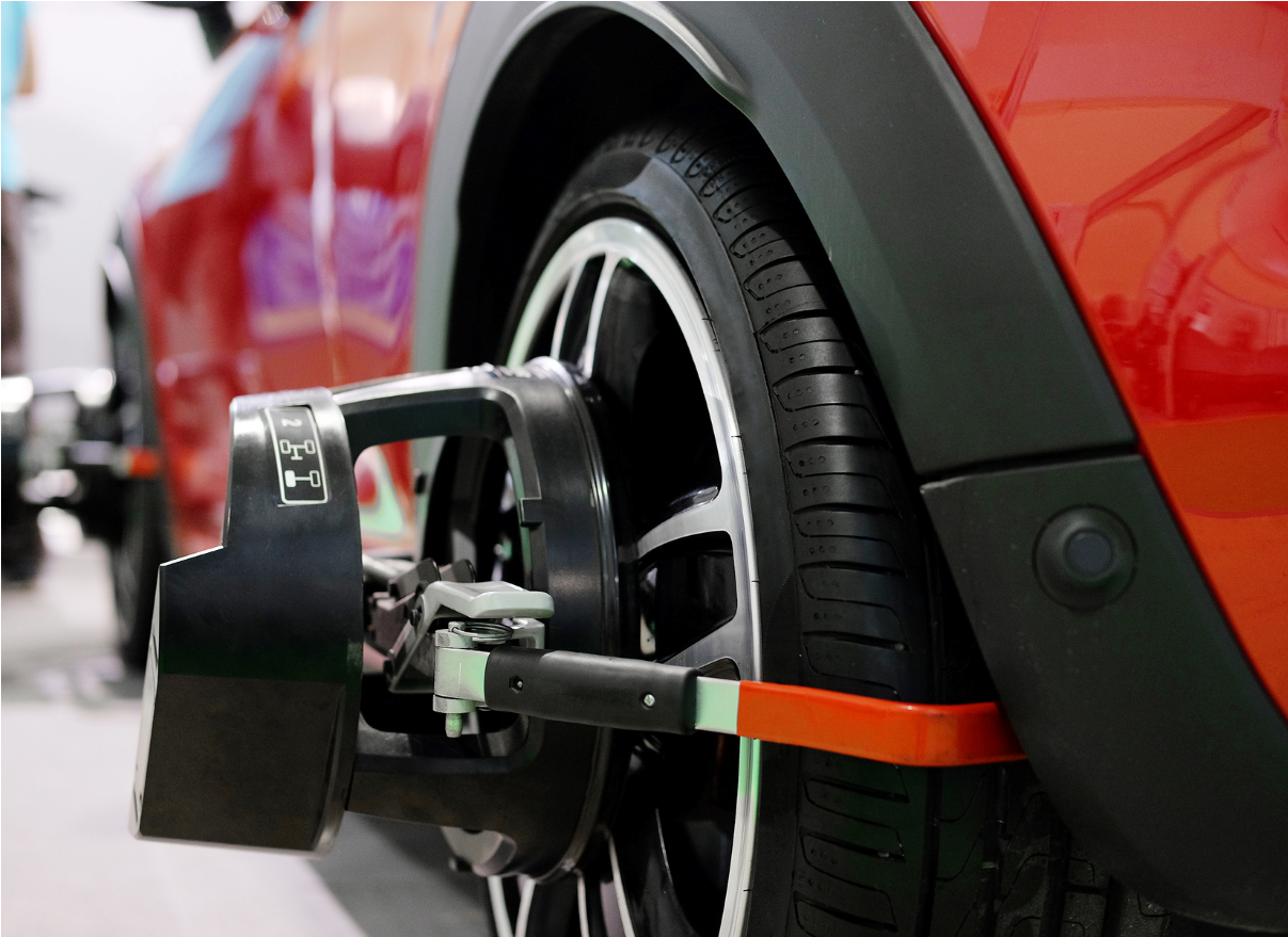Wheel alignment machine attached to a red car’s rear tire in a garage.