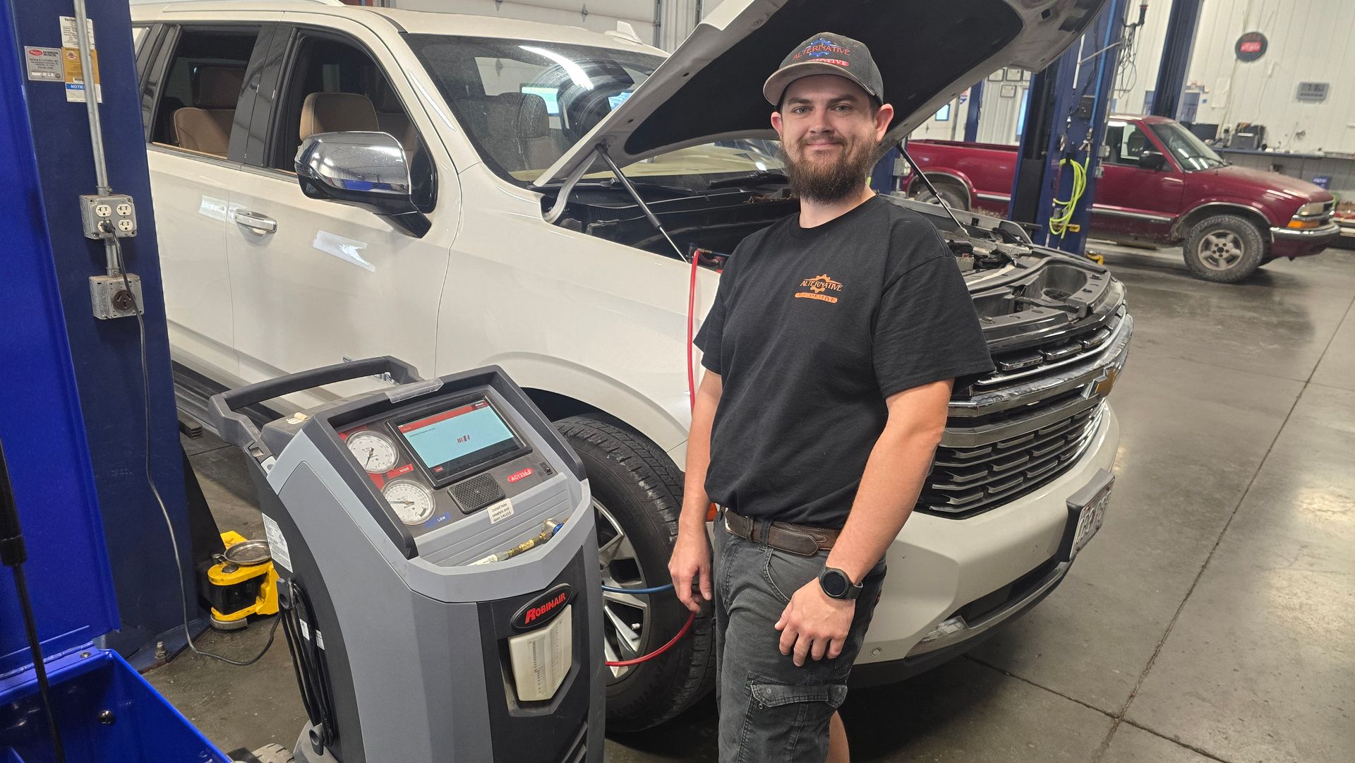 Mechanic standing beside a white SUV in an auto shop, with an AC machine in front of the open hood