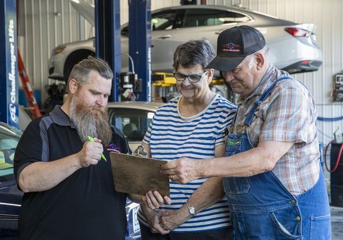 Three mechanics review a clipboard in an auto repair shop with a car on a lift