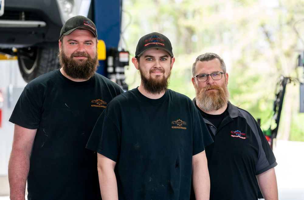 Three men in black shirts and caps stand outdoors, smiling at the camera.