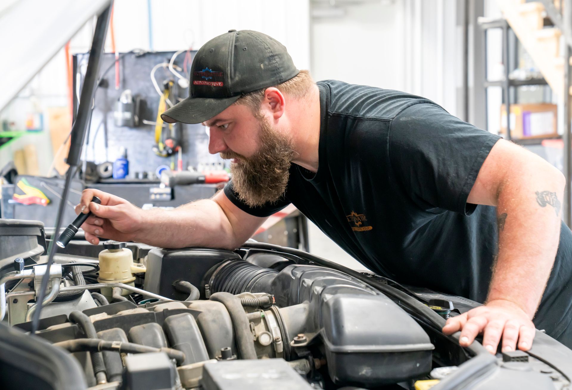 Mechanic inspecting a car engine in a garage with a tool in hand