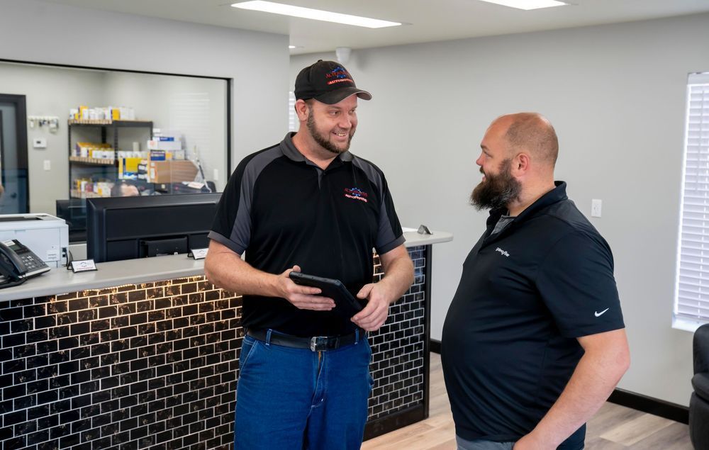 Two men in black polos talking in an office lobby, one holding a tablet.
