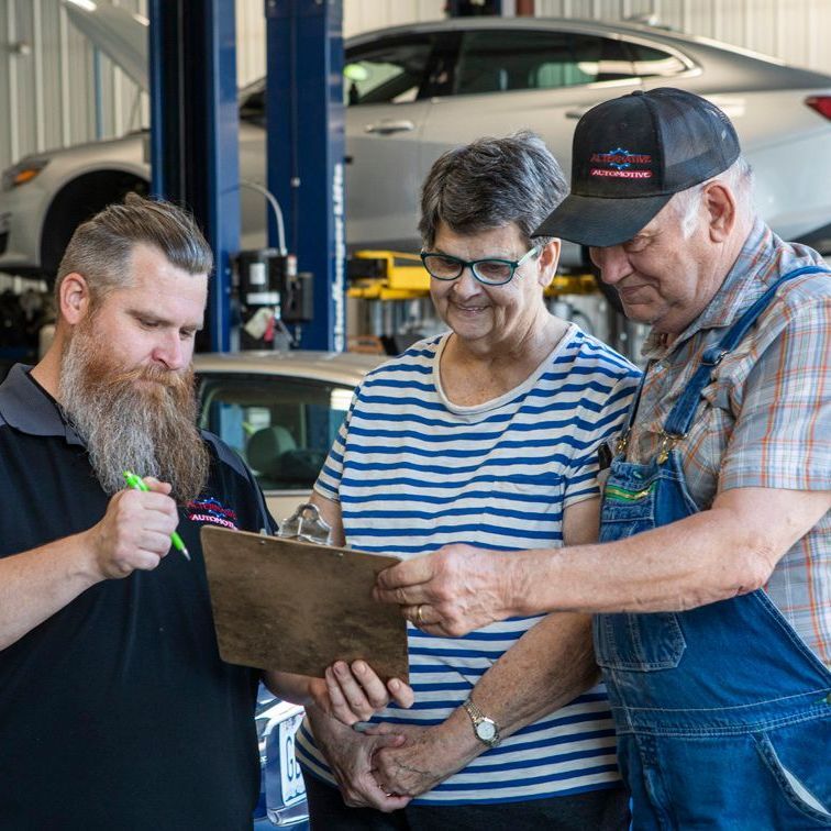 Three mechanics reviewing a clipboard together in an auto repair shop.