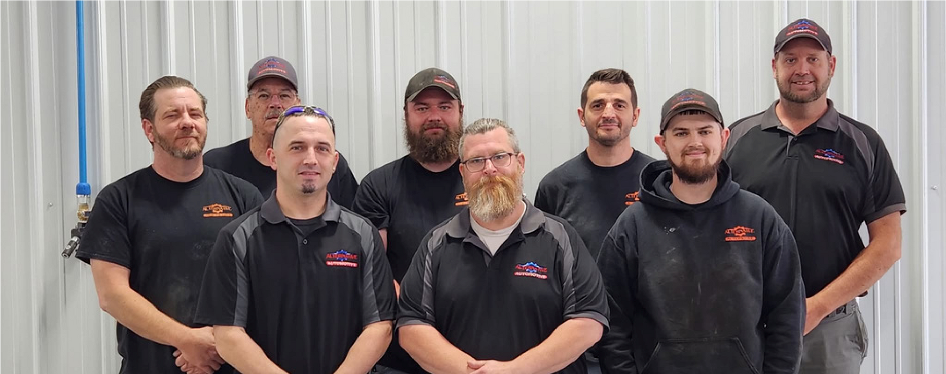 Seven workers in black shirts and caps posing indoors in front of a white corrugated wall