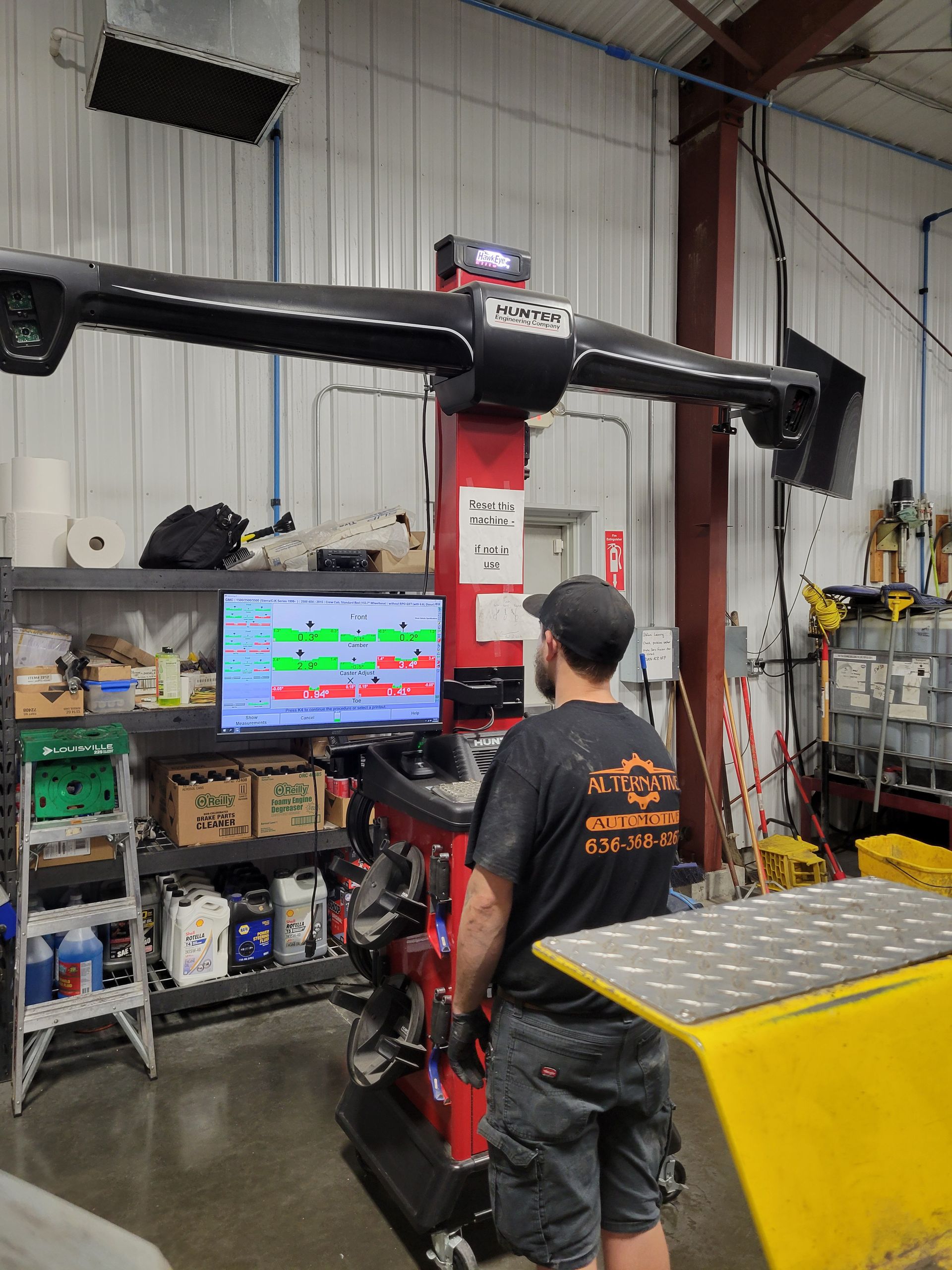 Person stands beside a large red hydraulic lift in a workshop garage, facing a computer monitor.