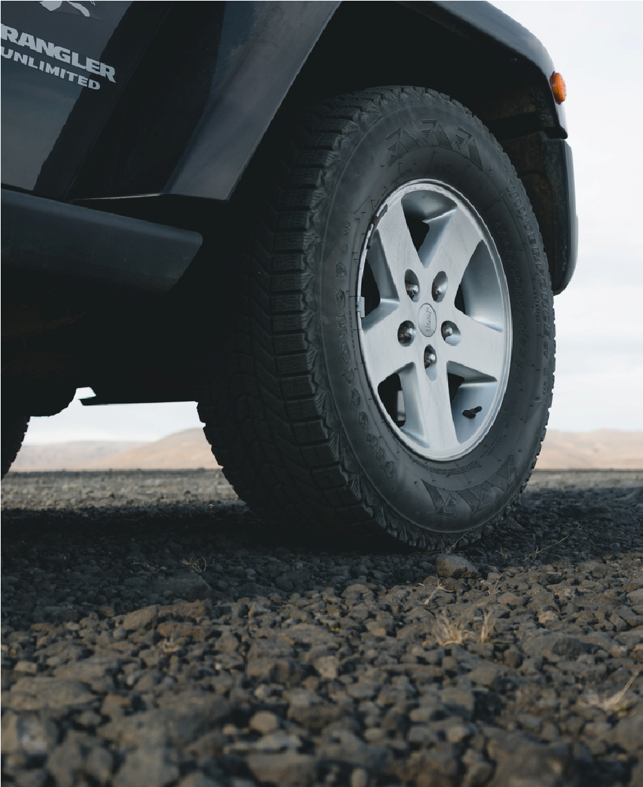Close-up of a car tire on a gravel road, with the vehicle’s dark body visible above.