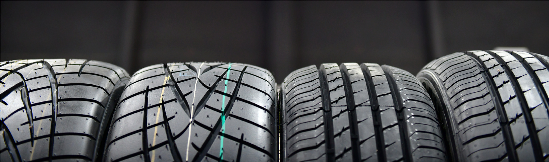 Row of black car tires with tread patterns against a dark background