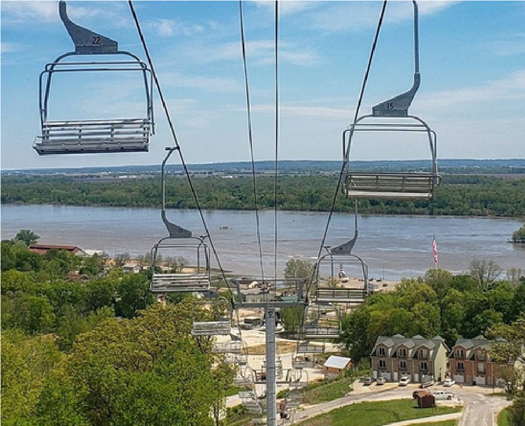 Empty chairlift gondolas over a river and green landscape on a clear day