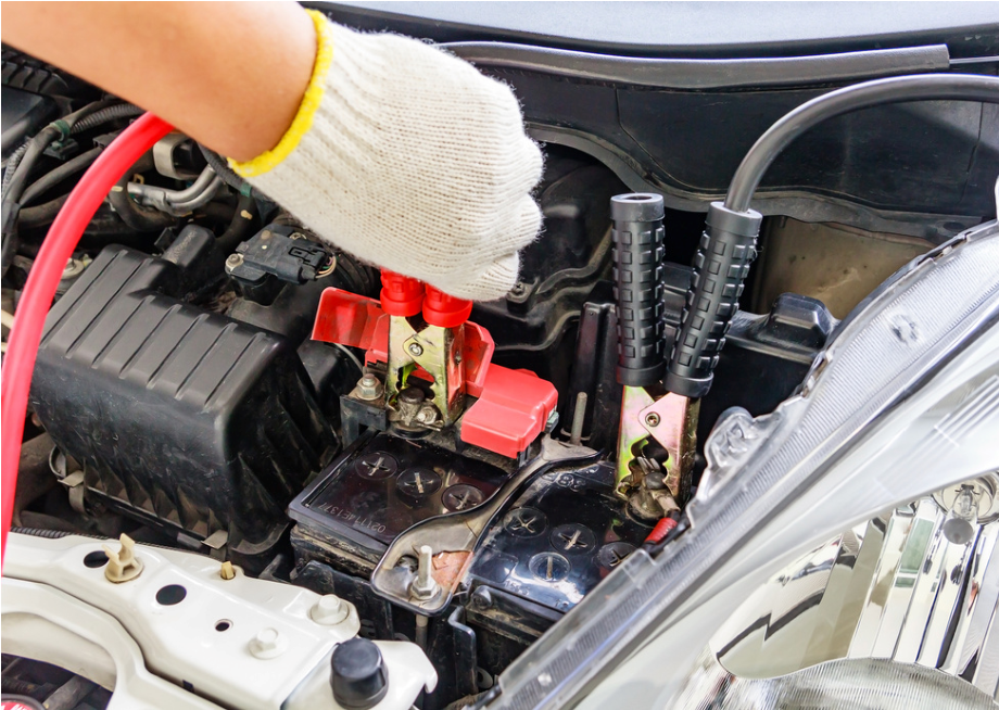 Gloved hand connects jumper cables to a car battery in an open engine bay