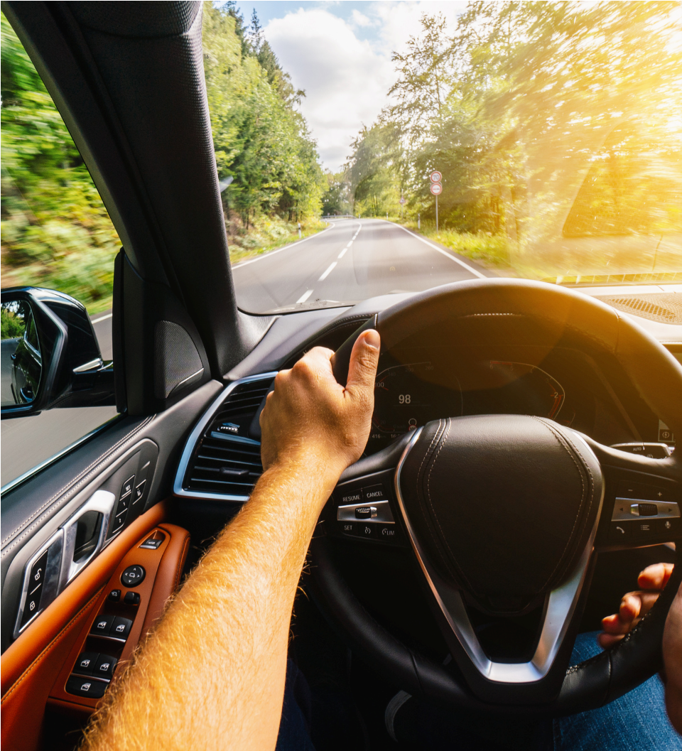 Driver’s view of hands on a steering wheel on a sunny road through trees