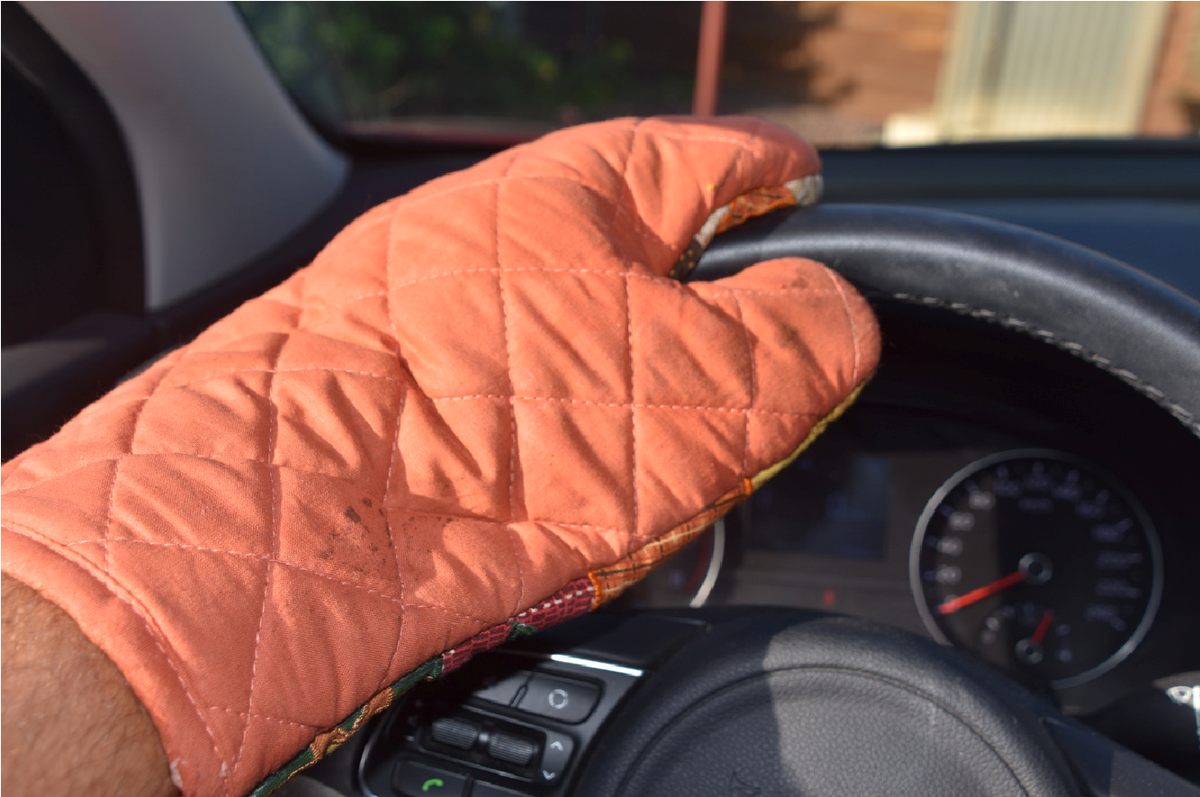 Orange quilted mitt resting on a steering wheel inside a car dashboard view
