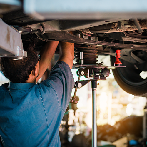Mechanic repairing a car’s suspension underneath a raised vehicle in a garage