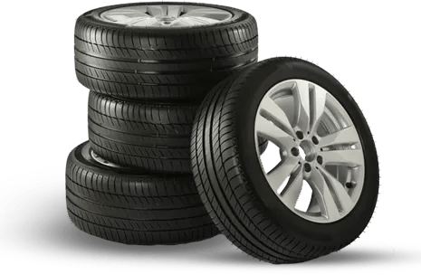 Stack of black car tires with one tire leaning in front, showing a silver alloy wheel.