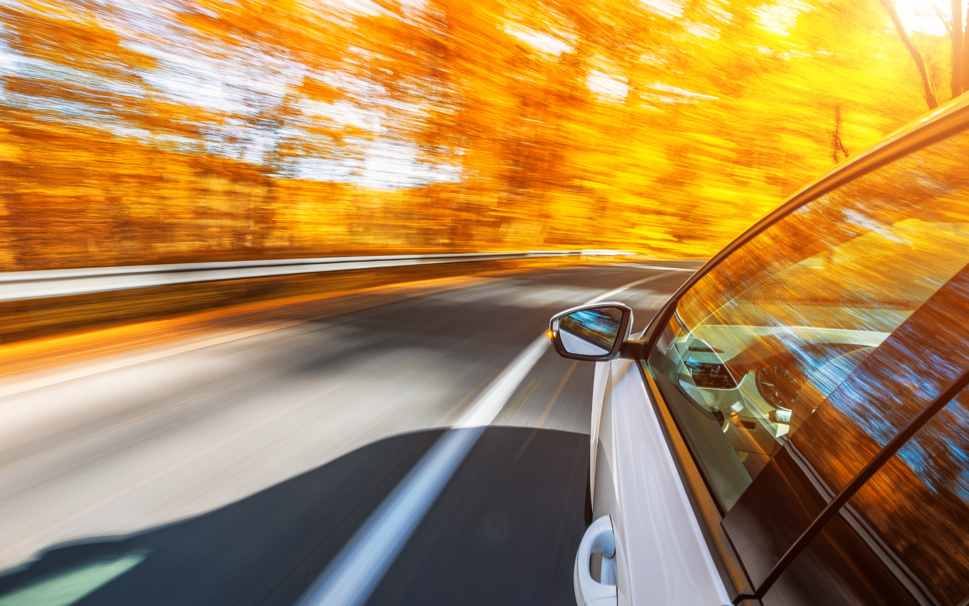 Car driving fast on a curving road through blurred autumn trees, seen from the side window