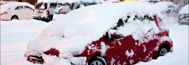 Red car buried under heavy snow in a snowy parking lot