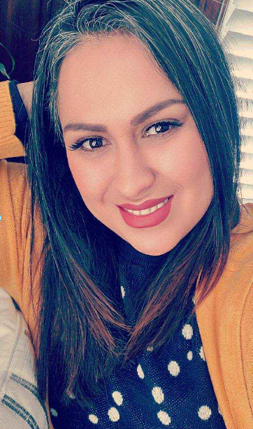 A woman wearing a yellow cardigan and a polka dot dress is smiling for the camera.