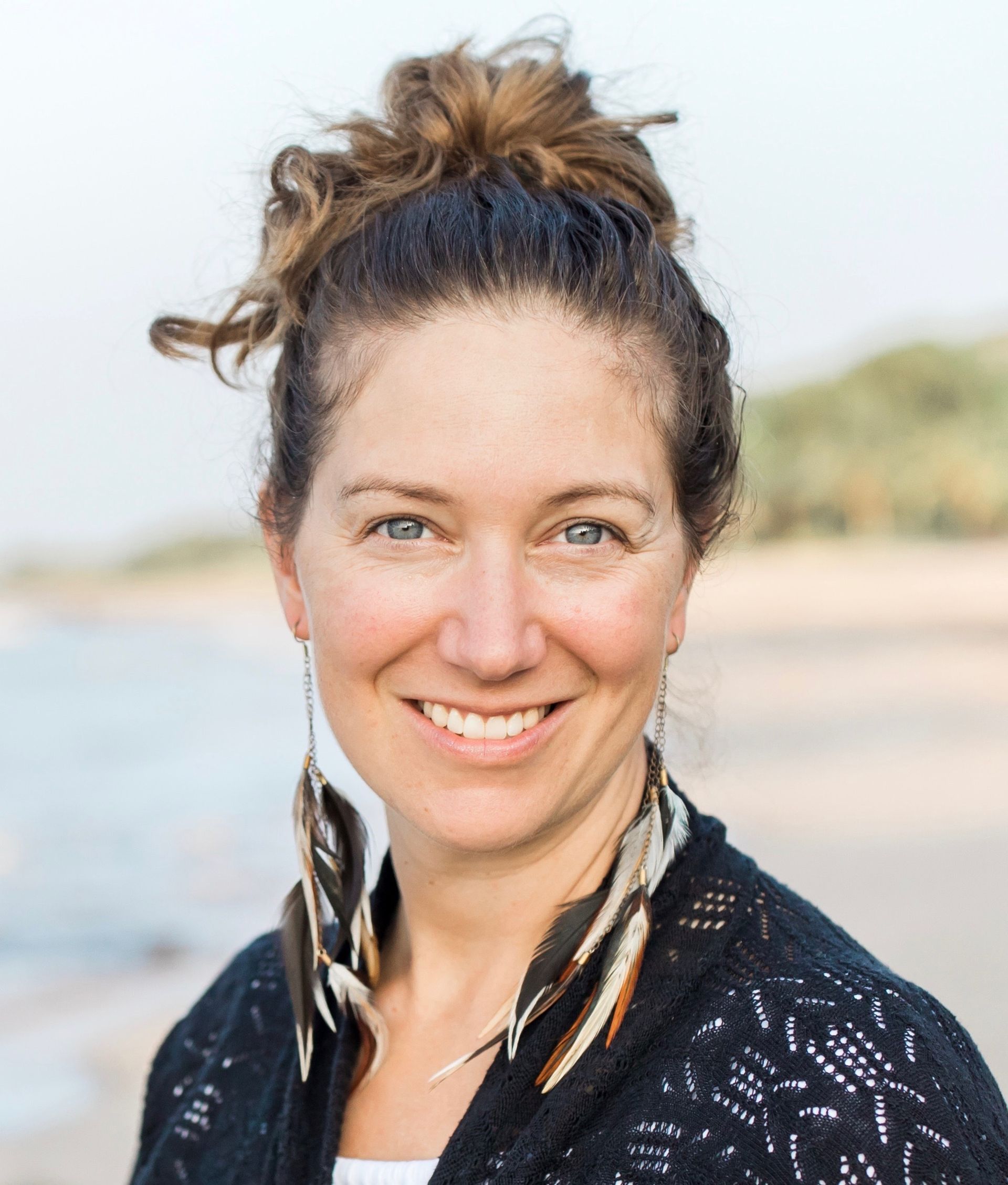 A woman wearing a black sweater and feather earrings is smiling for the camera.