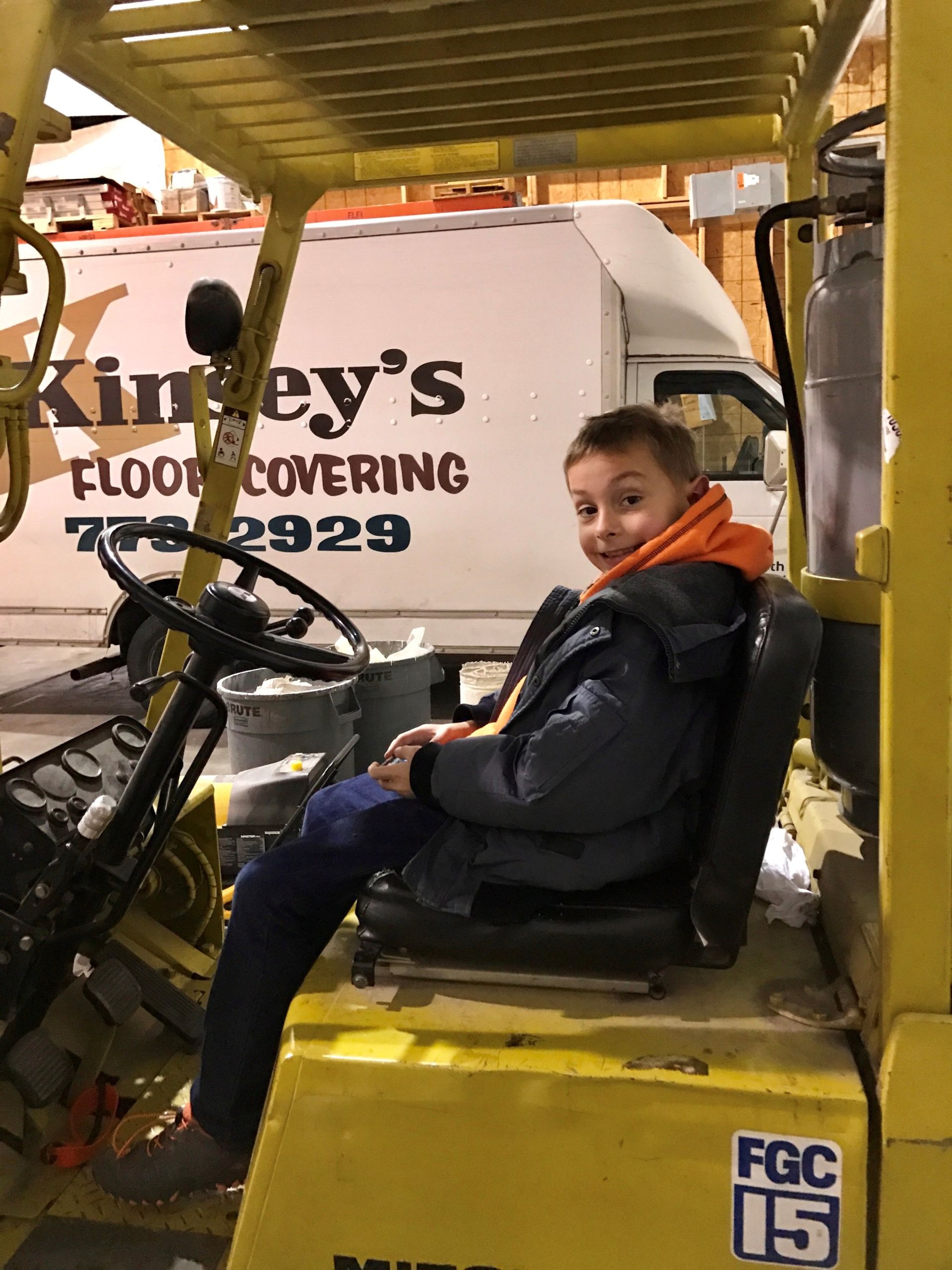Boy sitting in a forklift, smiling. Warehouse setting, truck with 