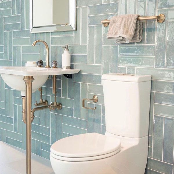 Blue-tiled bathroom with a pedestal sink, toilet, and gold fixtures; a towel hangs on the wall.