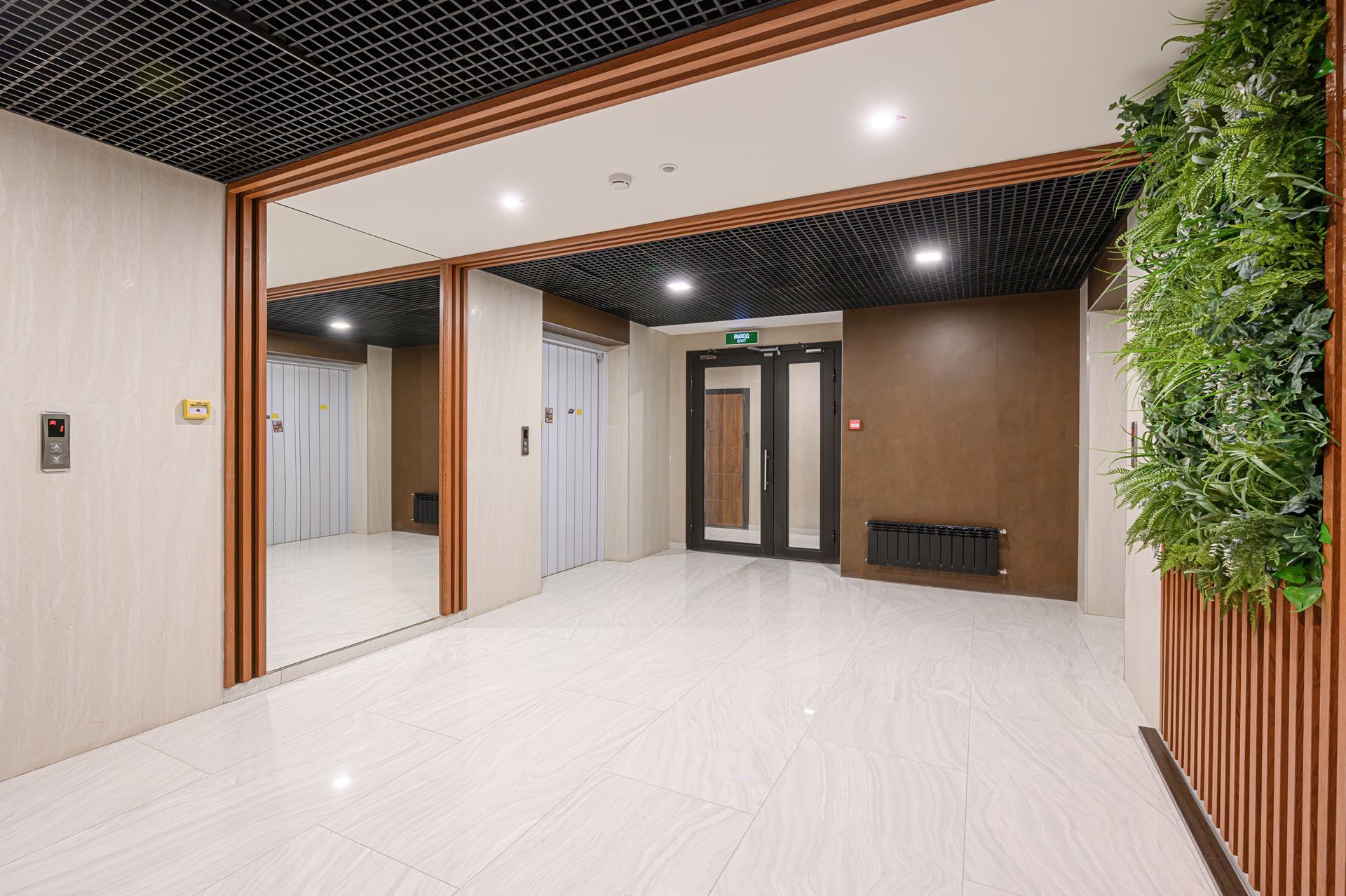 Modern lobby with white tile floor, wood slat ceiling, glass doors, and green vertical plant wall