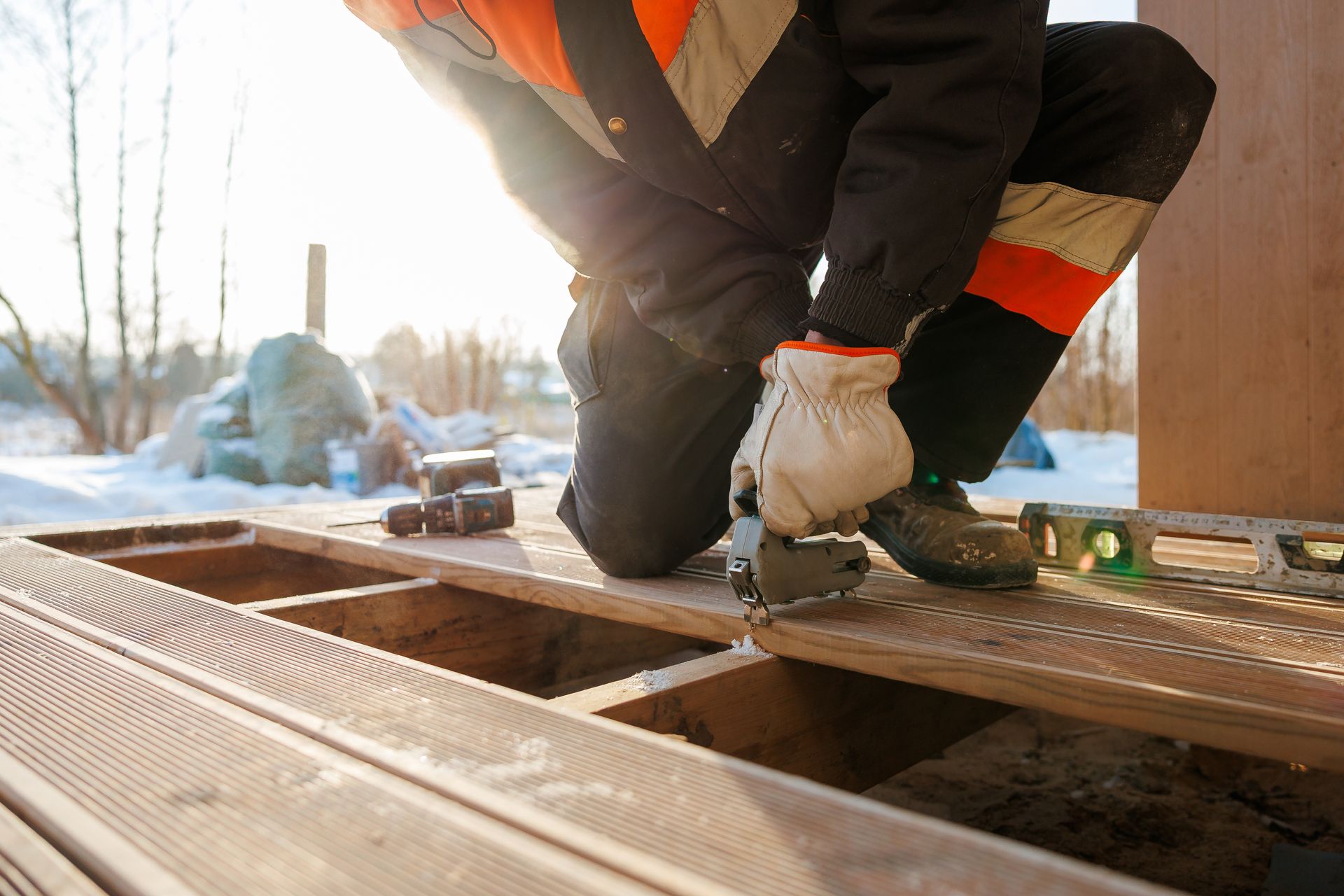 Worker kneeling on a rooftop, fastening metal decking in bright sunlight
