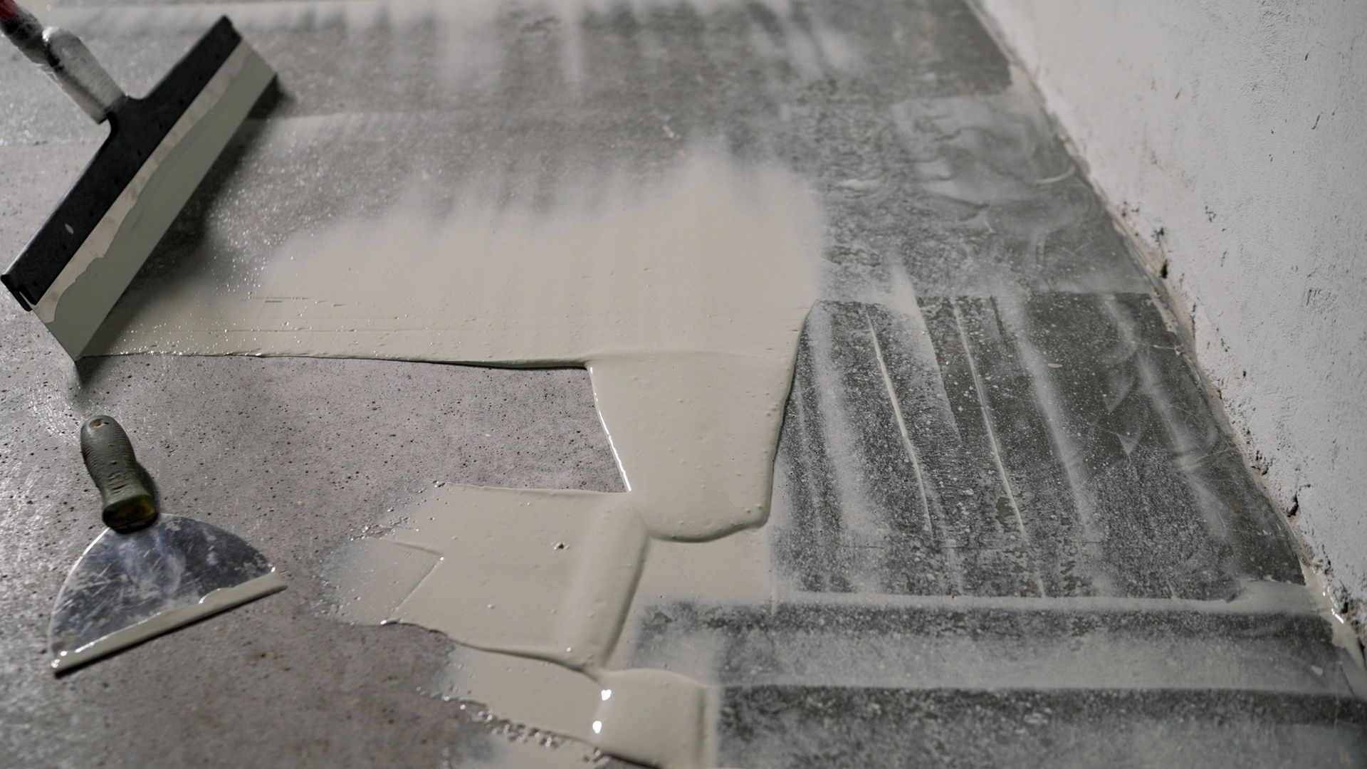 Concrete floor with fresh gray coating being spread by a trowel near a wall