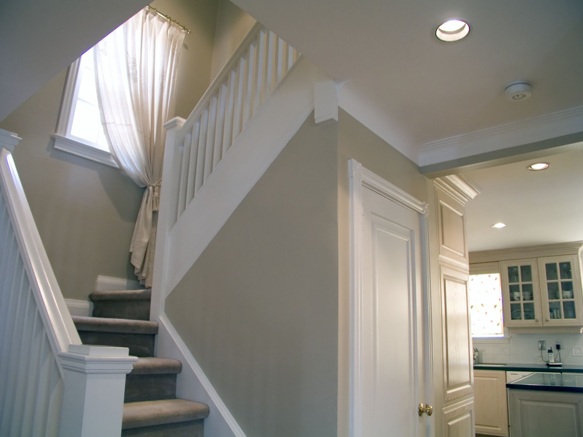 Bright hallway with carpeted staircase, white trim, and a view into a kitchen through an open doorway