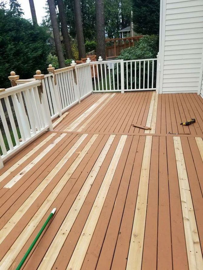 A wooden deck with alternating stained brown and raw light-colored planks, bordered by white railings against a house.