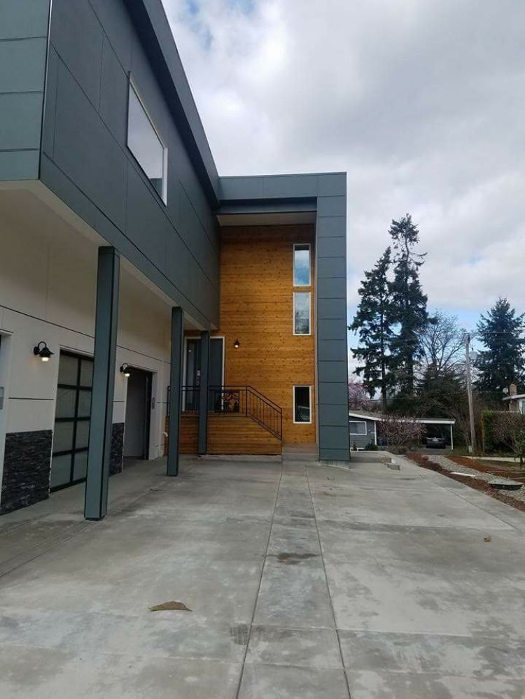Modern building exterior with concrete walkway, gray and wood siding, and trees in the background