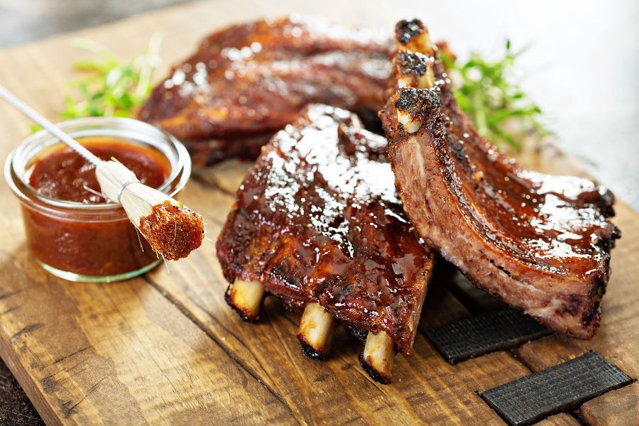 a wooden cutting board topped with ribs and a bowl of barbecue sauce .