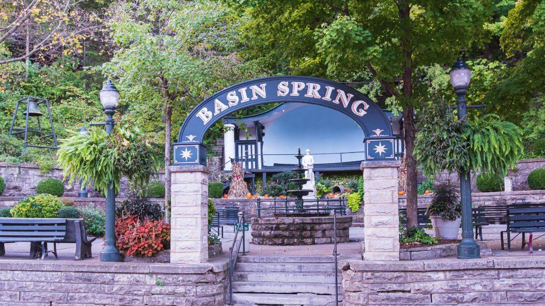 the entrance to basin spring park is surrounded by trees and benches .