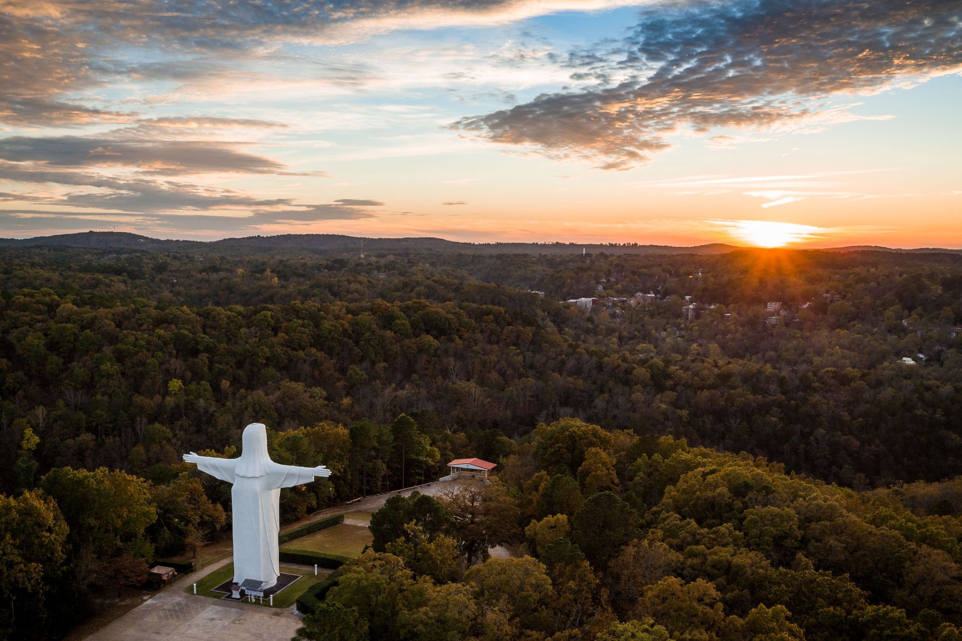 an aerial view of a statue of jesus surrounded by trees at sunset .