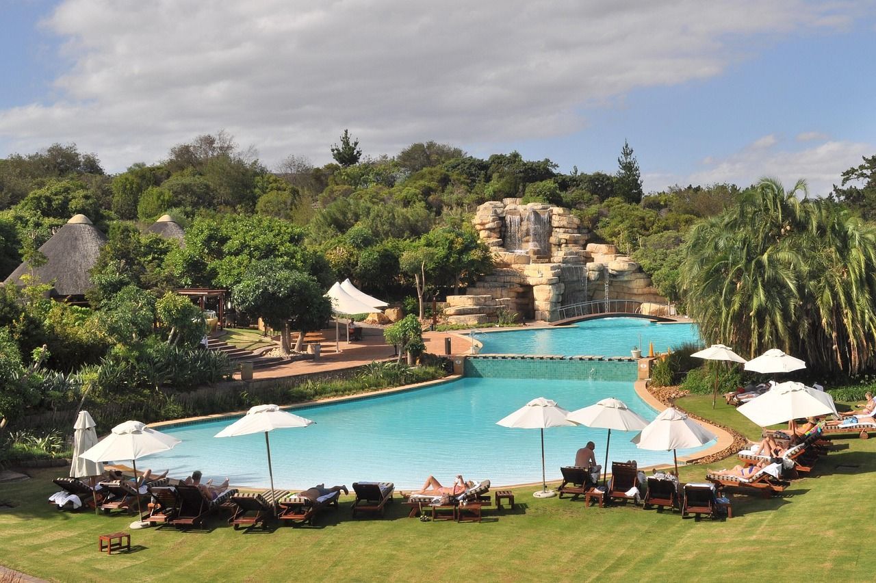 Swimming pool with waterfalls, umbrellas, and people sunbathing on a sunny day.