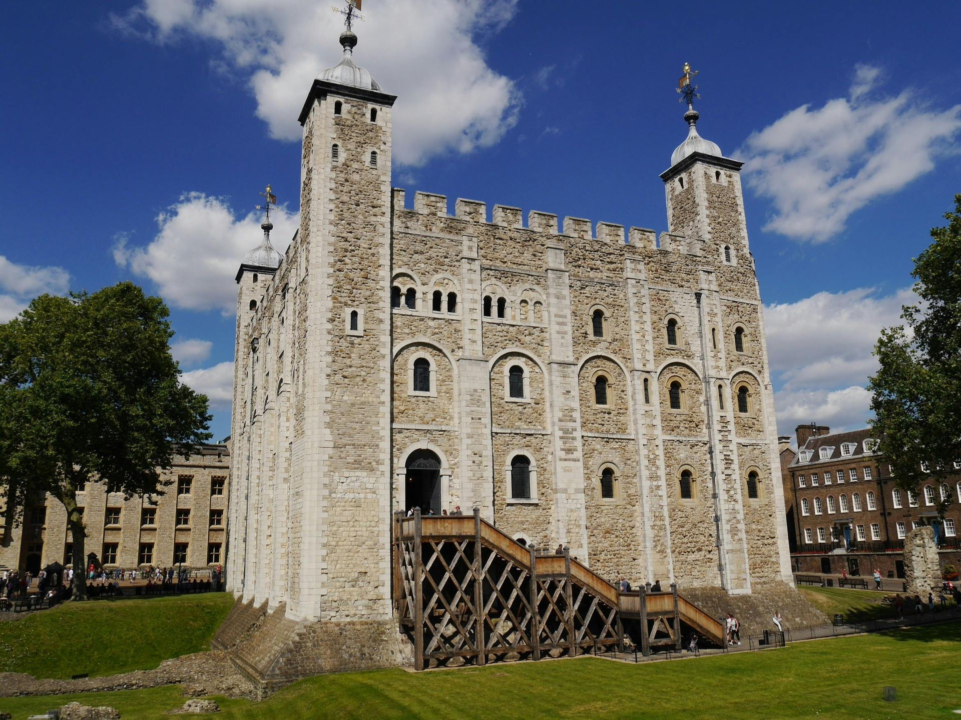 White Tower of the Tower of London, a medieval castle, against a blue sky with fluffy clouds. Wooden scaffolding on the entrance.